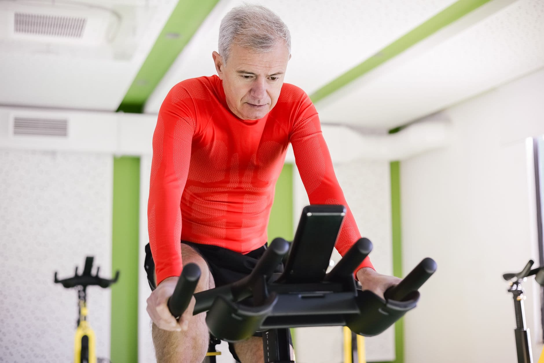homem idoso de roupa esportiva pedalando em bicicleta ergométrica