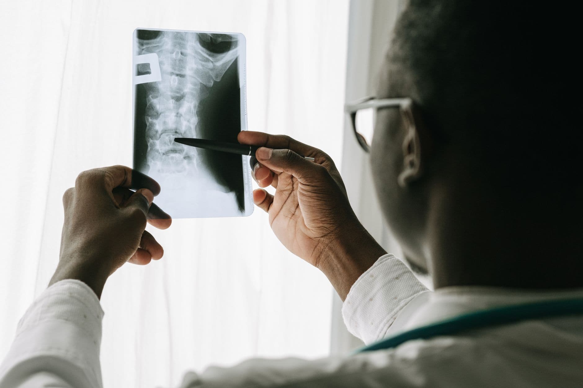 médico examinando uma radiografia da coluna com uma caneta na mão