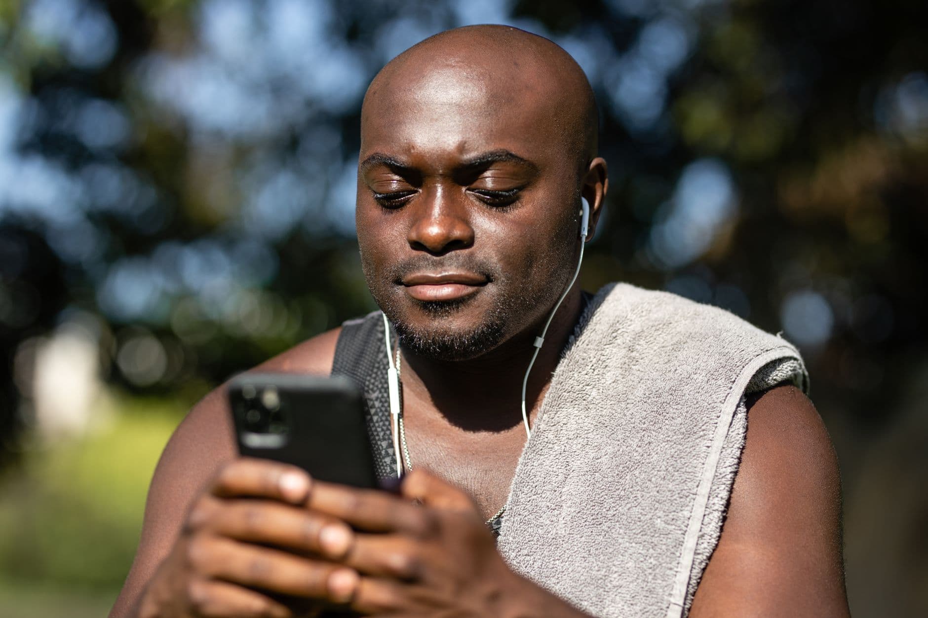 homem olhando para baixo para o celular, com fones e toalha no ombro