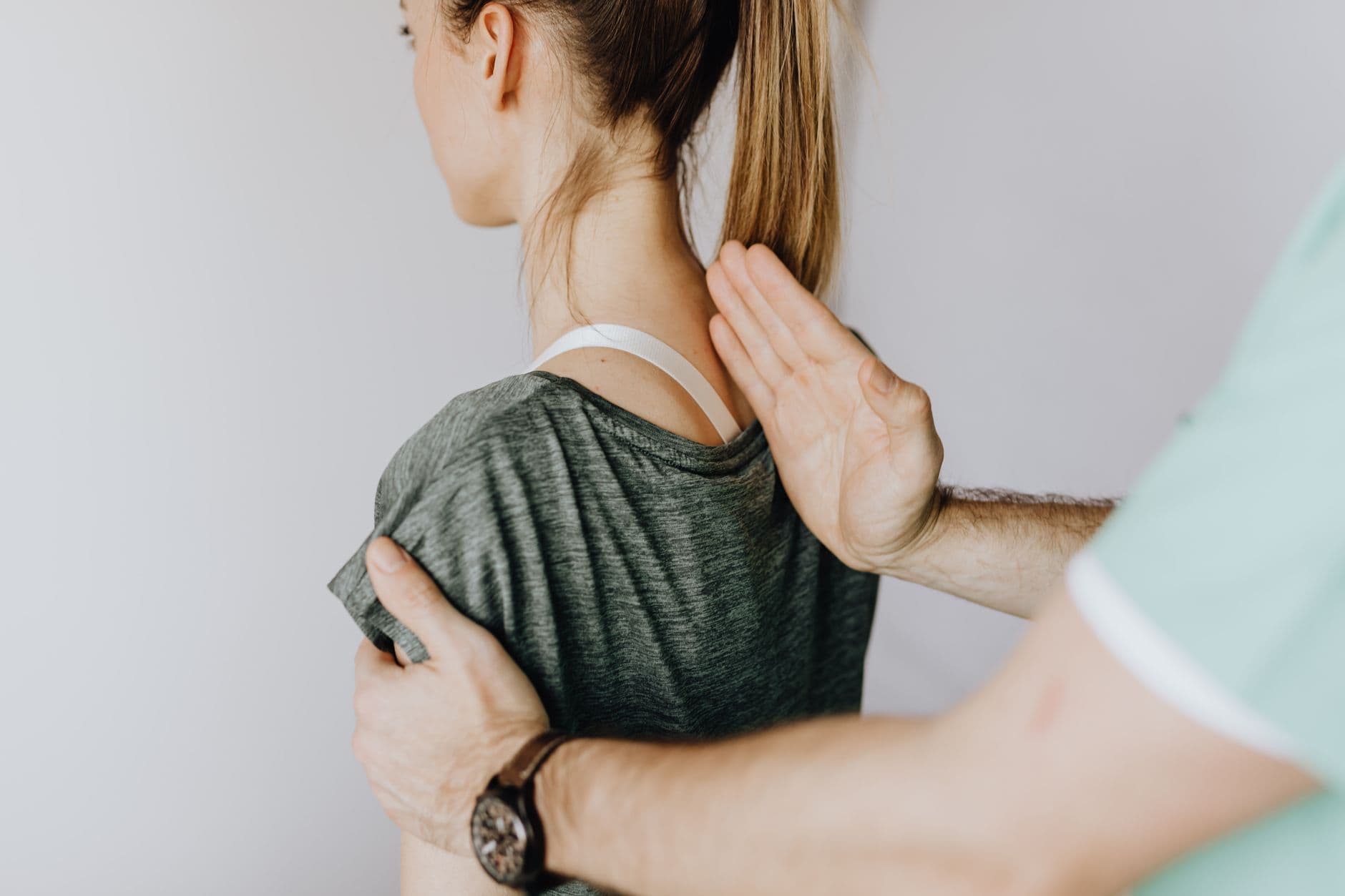 profissional apoiando as mãos nas costas de uma mulher, entre as escápulas, durante avaliação
