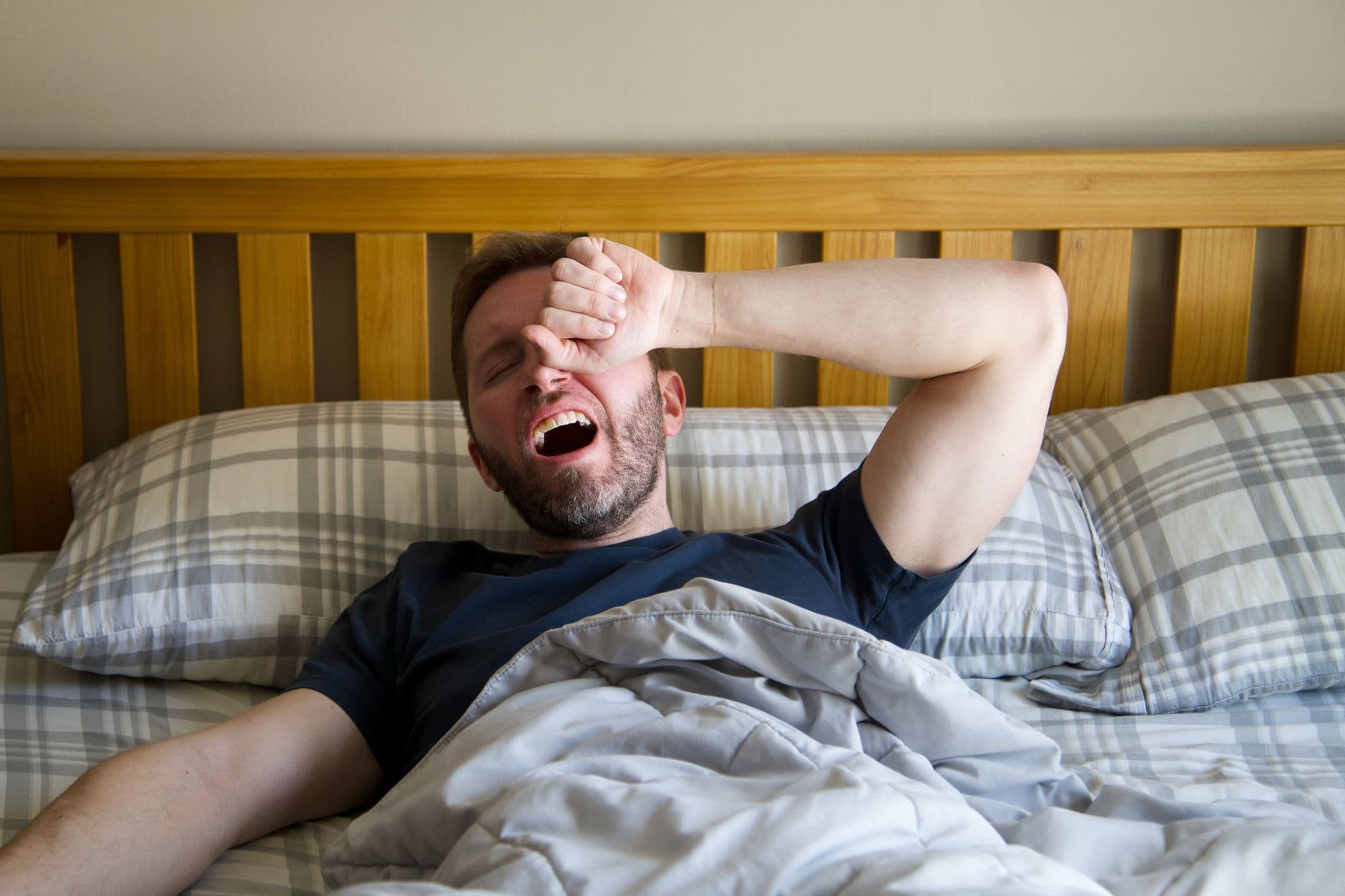 homem bocejando ao acordar na cama, com a mão na testa