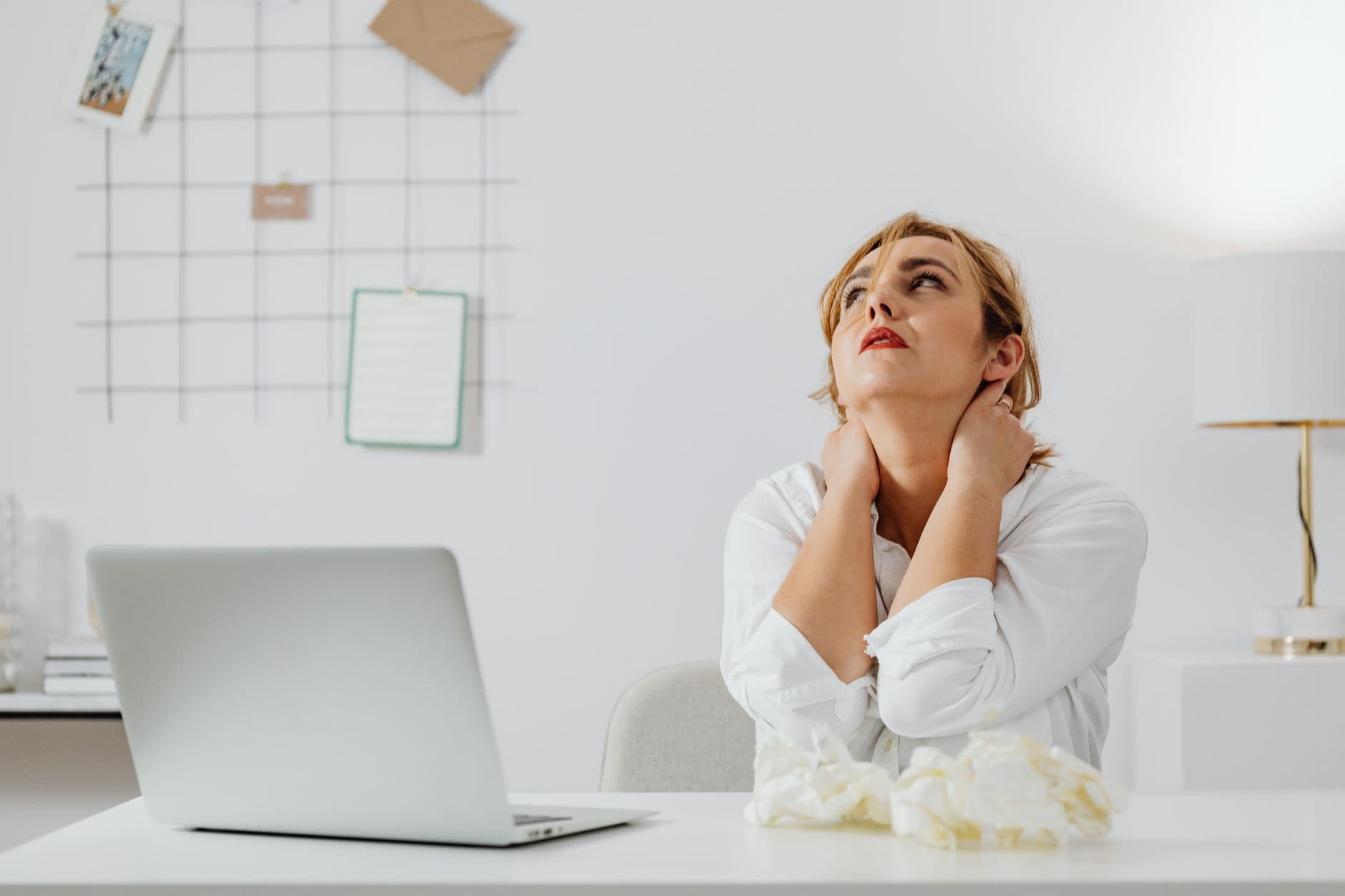 mulher sentada à mesa com notebook levando as duas mãos à nuca