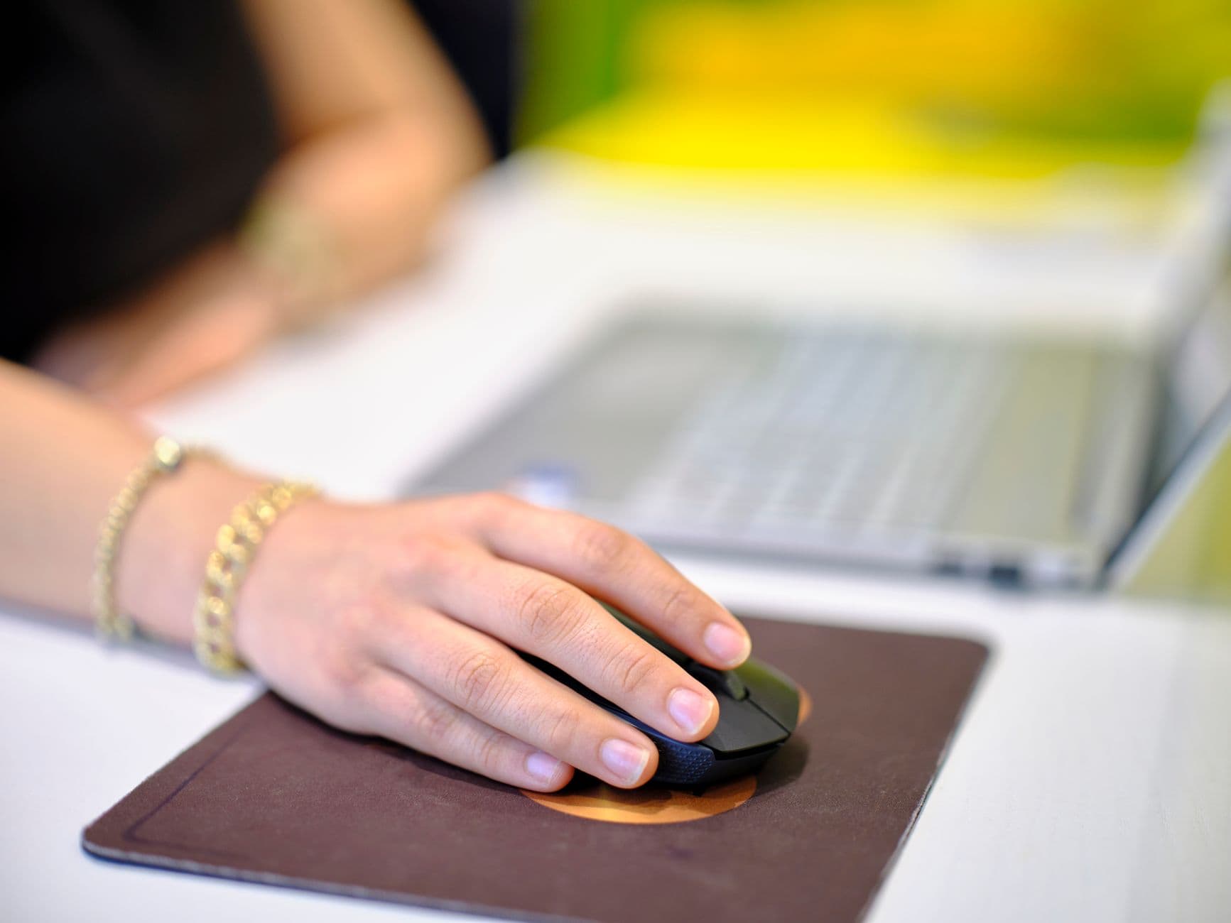 mão de mulher sobre o mouse ao lado de um notebook