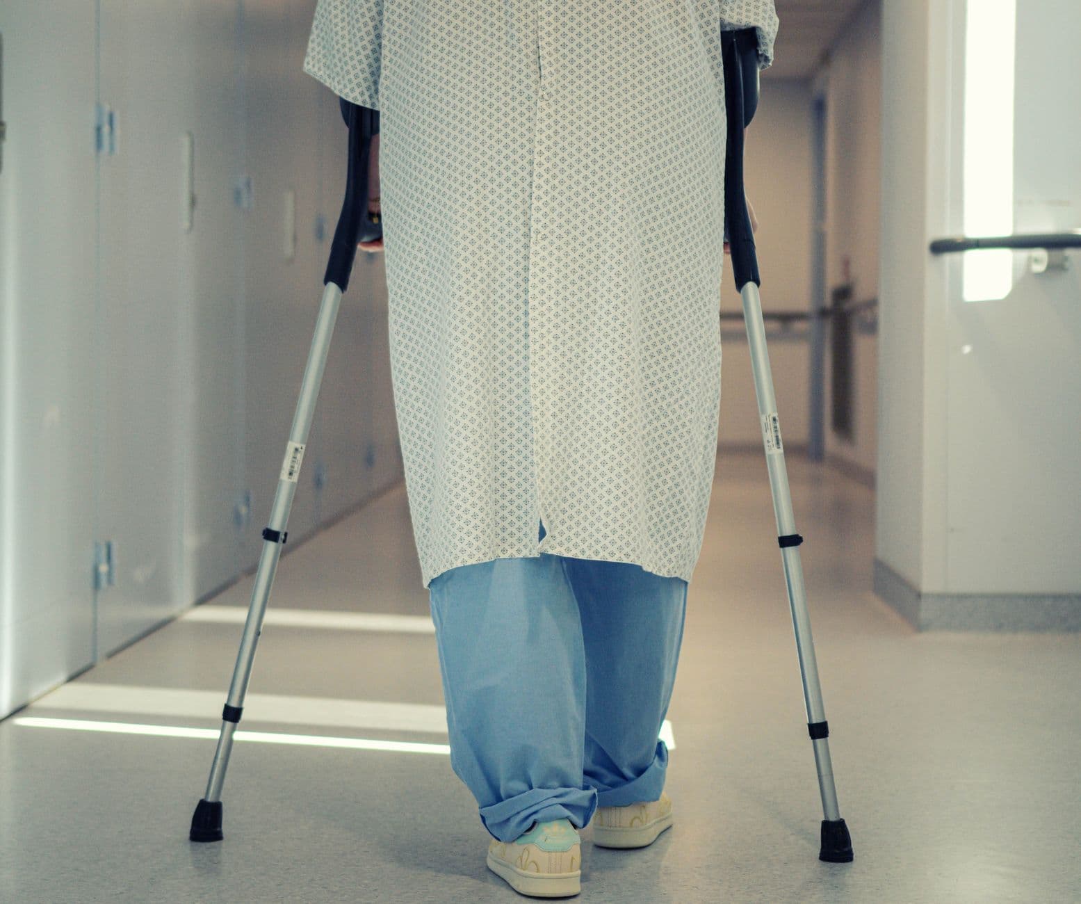 pessoa idosa caminhando de muletas pelo corredor de um hospital