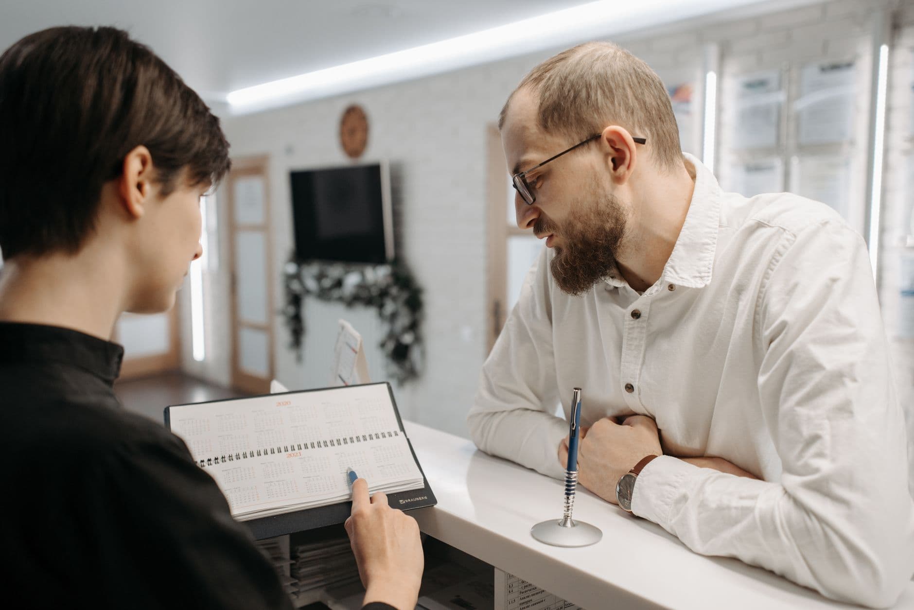 recepcionista mostrando a agenda a um homem apoiado no balcão de uma clínica