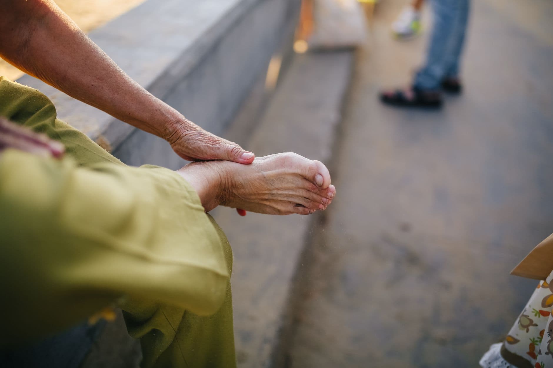 pessoa idosa sentada ao ar livre massageando o próprio pé